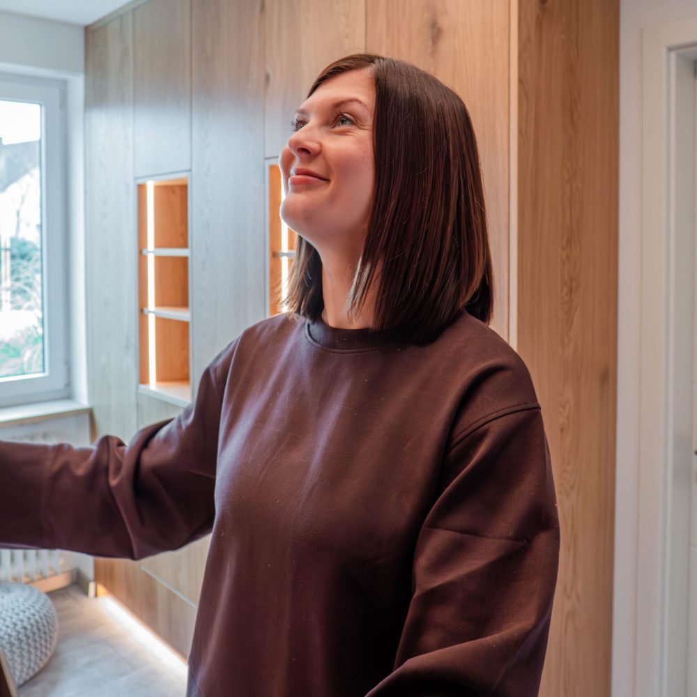 Kunden Testimonial steht vor maßgefertigtem Einbauschrank aus Holz mit integrierter Beleuchtung