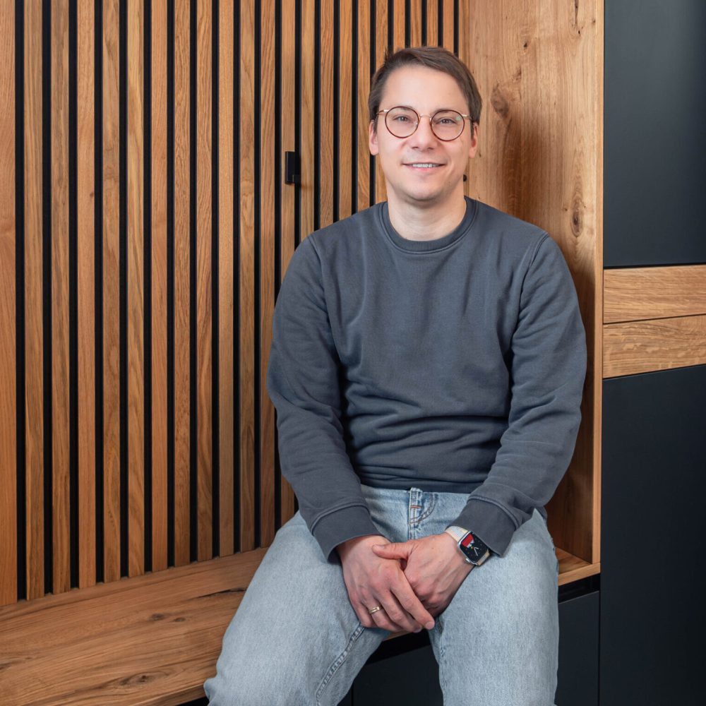 Mann sitzt auf maßgefertigter Garderobe mit Lamellenwand und integrierter Sitzbank