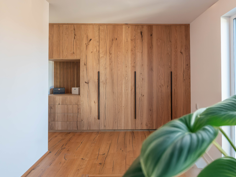 Wandfüllender maßgefertigter Einbauschrank aus rustikaler Eiche mit langen schwarzen Griffen, Schubladen und offener Nische.