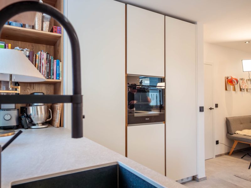 Moderne maßgefertigte Küche mit weißen grifflosen Fronten, Holzakzenten, Einbaubackofen und offenem Regal.