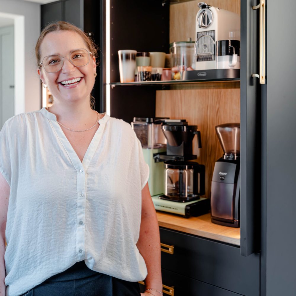 Kunden Testimonial steht vor maßgefertigtem Küchenschrank mit integrierter Gerätenische und Stauraum