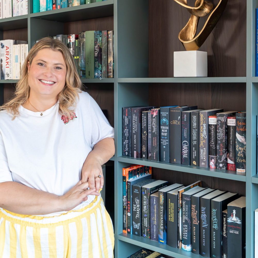 Kundin steht vor maßgefertigtem Bücherregal mit farblich sortierten Büchern im Wohnbereich